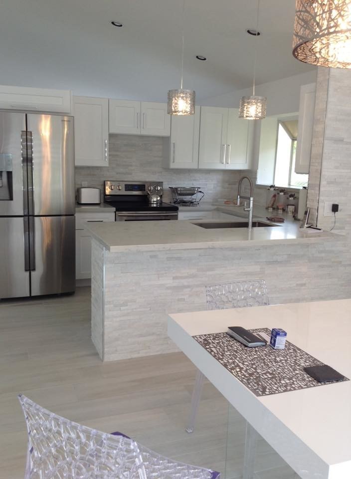 Small contemporary u-shaped kitchen in Miami with a single-bowl sink, shaker cabinets, white cabinets, engineered stone countertops, white splashback and stainless steel appliances.