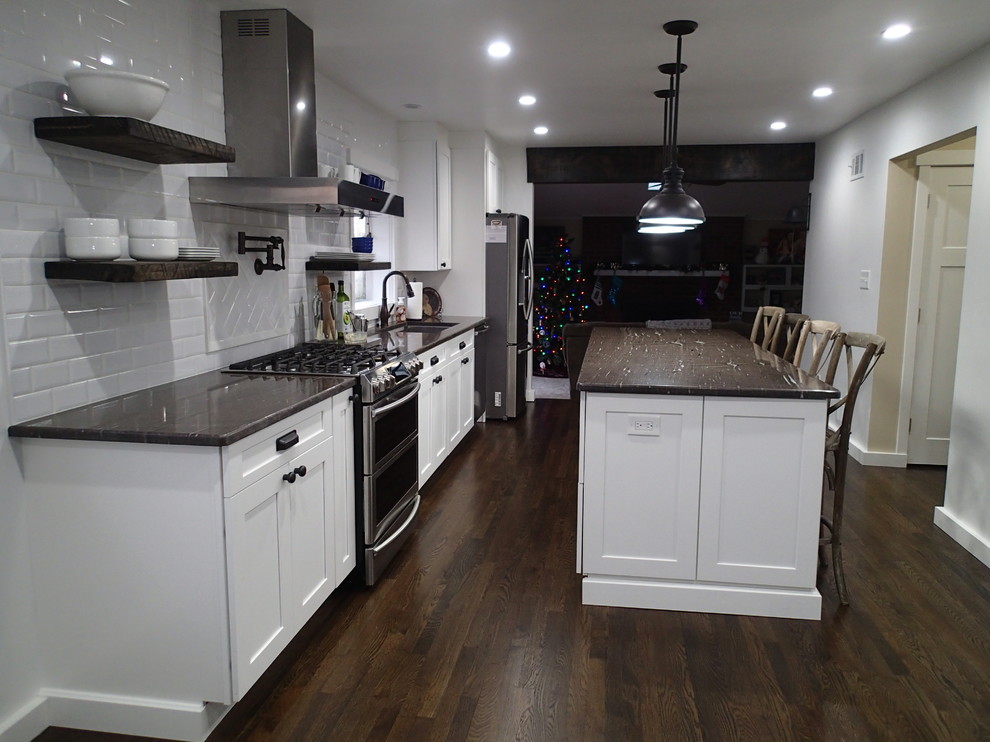 Industriell inredning av ett mellanstort brun brunt kök, med en undermonterad diskho, skåp i shakerstil, vita skåp, granitbänkskiva, vitt stänkskydd, stänkskydd i tunnelbanekakel, rostfria vitvaror, mörkt trägolv, en köksö och brunt golv