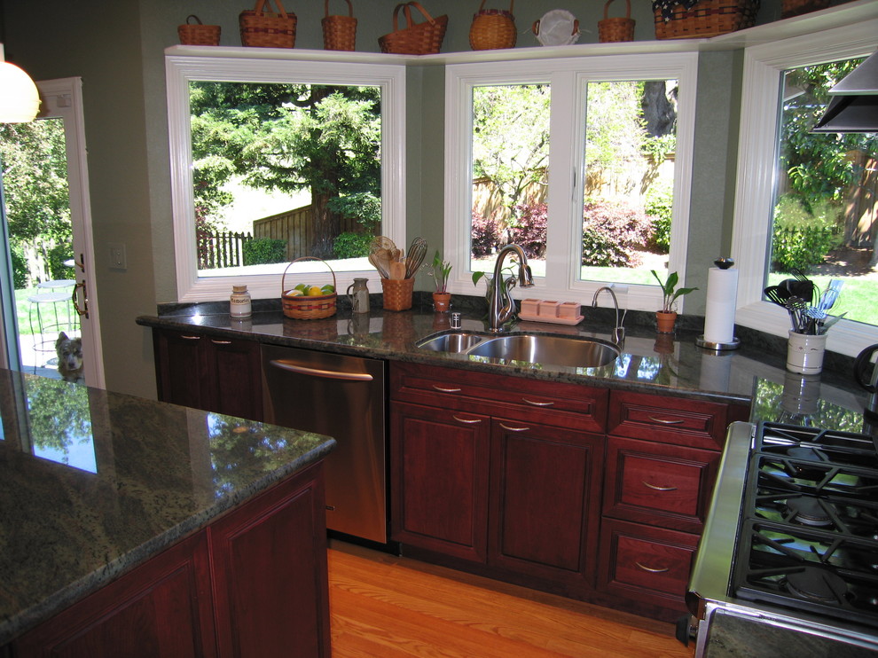 Klassisk inredning av ett avskilt, stort u-kök, med en undermonterad diskho, luckor med upphöjd panel, skåp i mörkt trä, granitbänkskiva, grönt stänkskydd, stänkskydd i sten, rostfria vitvaror, mellanmörkt trägolv och en köksö