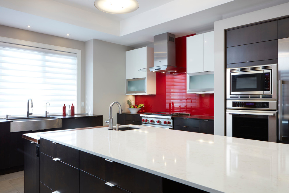 Inspiration for a large contemporary l-shaped kitchen in Toronto with a belfast sink, flat-panel cabinets, dark wood cabinets, engineered stone countertops, red splashback, glass sheet splashback, stainless steel appliances, travertine flooring and an island.