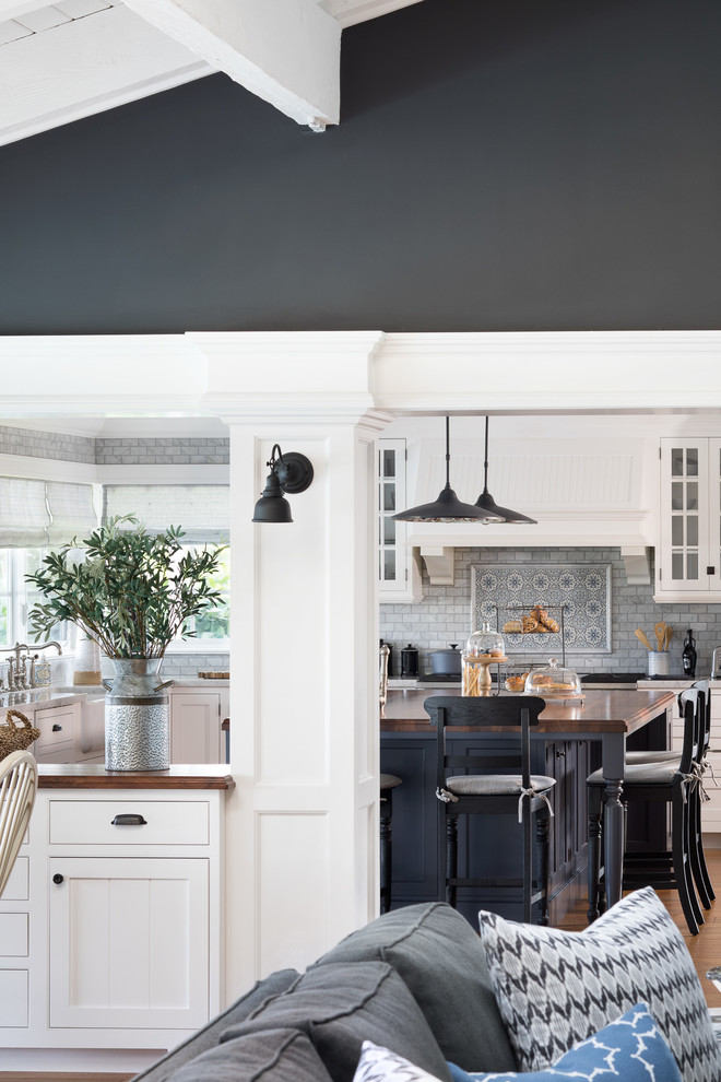 Inspiration for a mid-sized coastal u-shaped medium tone wood floor and brown floor open concept kitchen remodel in Miami with a farmhouse sink, white cabinets, gray backsplash, marble backsplash, paneled appliances, an island, recessed-panel cabinets and wood countertops