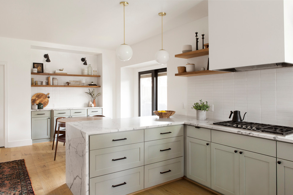 На фото: угловая кухня в скандинавском стиле с обеденным столом, фасадами в стиле шейкер, серыми фасадами, белым фартуком, светлым паркетным полом, полуостровом, бежевым полом и белой столешницей
