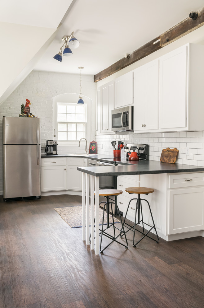 Bild på ett vintage grå grått l-kök, med en undermonterad diskho, skåp i shakerstil, vita skåp, vitt stänkskydd, stänkskydd i tunnelbanekakel, rostfria vitvaror, mellanmörkt trägolv och brunt golv