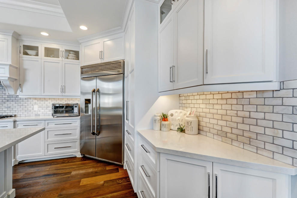 Bild på ett avskilt, stort vintage vit vitt u-kök, med en dubbel diskho, luckor med infälld panel, vita skåp, bänkskiva i kvarts, vitt stänkskydd, stänkskydd i marmor, rostfria vitvaror, mellanmörkt trägolv, en köksö och brunt golv
