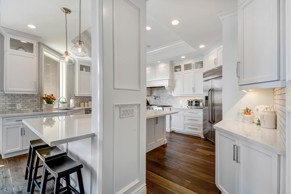 Inspiration for a large classic u-shaped enclosed kitchen in Los Angeles with recessed-panel cabinets, white cabinets, engineered stone countertops, white splashback, marble splashback, stainless steel appliances, an island, white worktops, a double-bowl sink, medium hardwood flooring and brown floors.