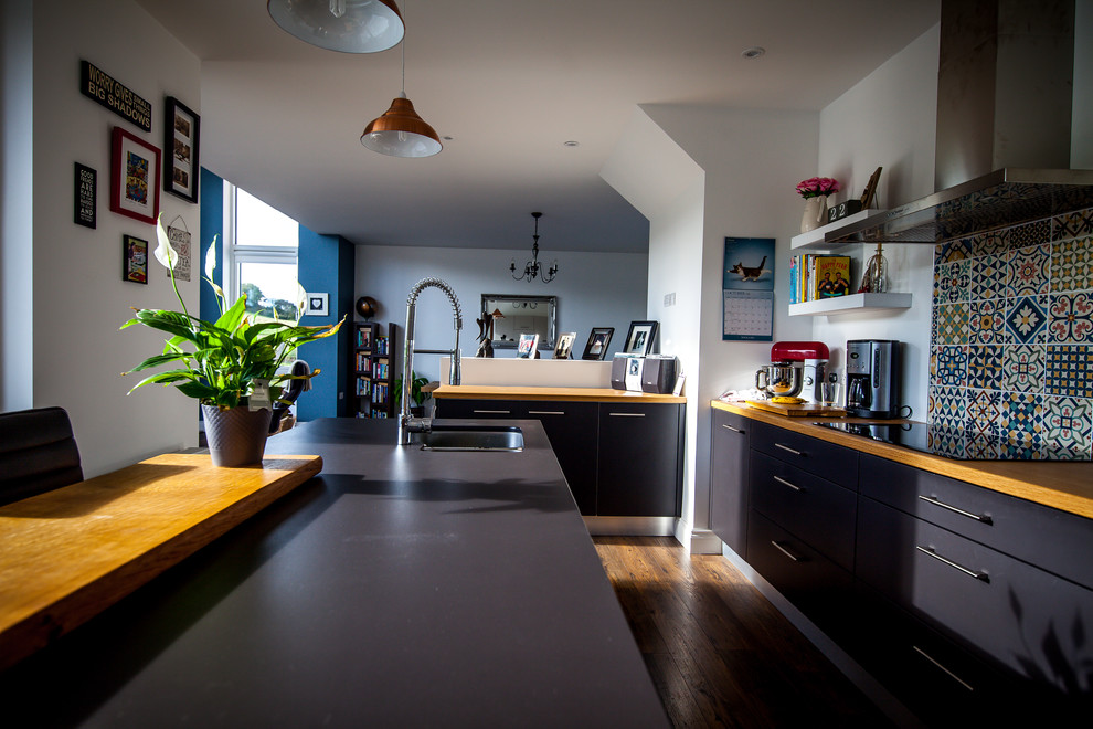 Modern inredning av ett kök, med en nedsänkt diskho, svarta skåp, träbänkskiva, flerfärgad stänkskydd, stänkskydd i keramik, integrerade vitvaror, mörkt trägolv och en halv köksö