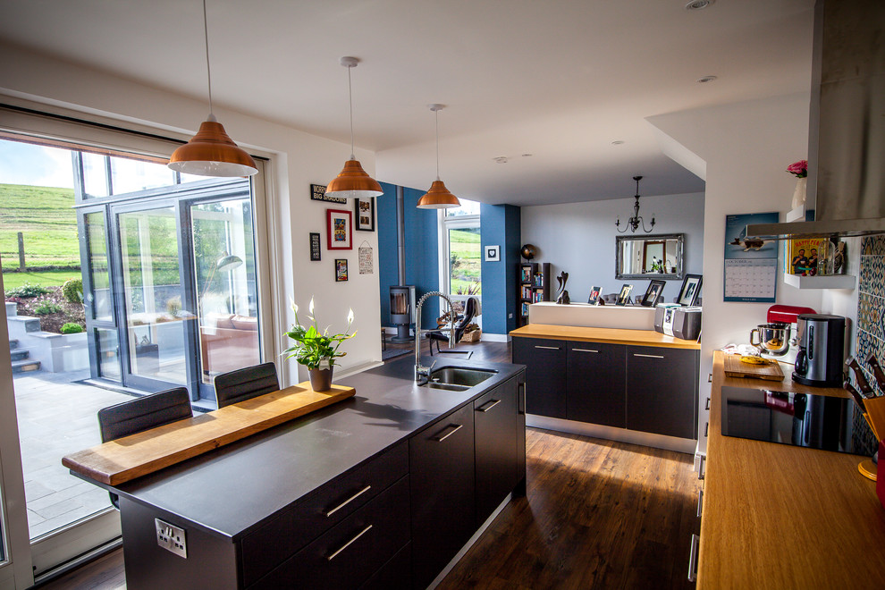 Contemporary kitchen in Cork with a built-in sink, black cabinets, wood worktops, multi-coloured splashback, ceramic splashback, integrated appliances, dark hardwood flooring and a breakfast bar.