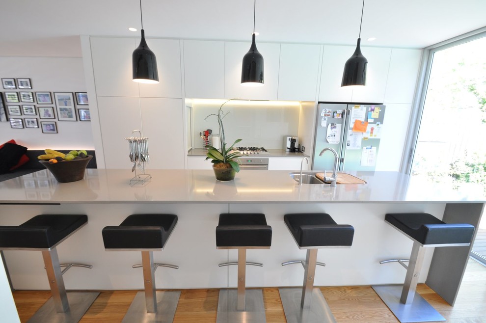 Foto på ett mellanstort funkis kök, med en dubbel diskho, släta luckor, vita skåp, rostfria vitvaror, ljust trägolv och en köksö