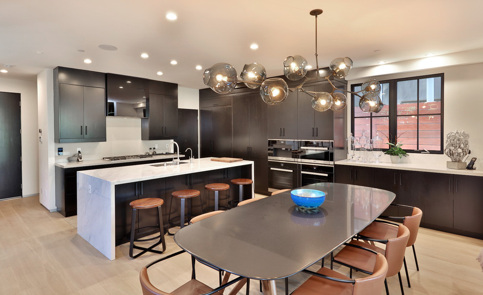 Photo of a contemporary l-shaped kitchen/diner in Los Angeles with a submerged sink, flat-panel cabinets, black cabinets, marble worktops, light hardwood flooring, an island and black appliances.