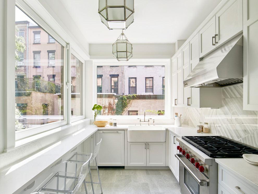 Example of a transitional l-shaped gray floor enclosed kitchen design in New York with a farmhouse sink, shaker cabinets, white cabinets, gray backsplash, stainless steel appliances, no island and white countertops