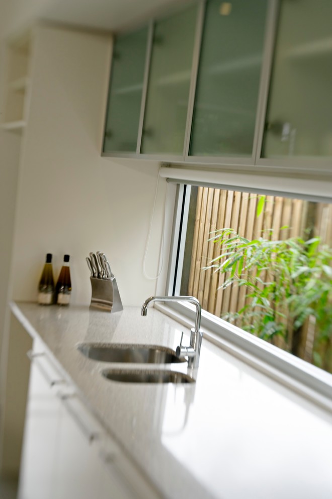 Immagine di una cucina minimal di medie dimensioni con lavello sottopiano, ante di vetro, ante bianche, top in quarzo composito, paraspruzzi con lastra di vetro, elettrodomestici in acciaio inossidabile e pavimento in gres porcellanato
