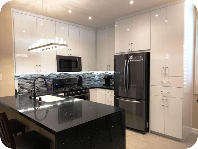 Small modern l-shaped open plan kitchen with a submerged sink, flat-panel cabinets, white cabinets, engineered stone countertops, multi-coloured splashback, matchstick tiled splashback, black appliances, laminate floors, a breakfast bar, beige floors and black worktops.