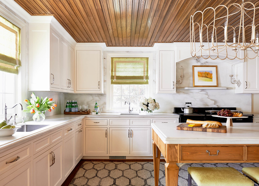 Exempel på ett stort klassiskt l-kök, med luckor med infälld panel, vita skåp, marmorbänkskiva, vitt stänkskydd, stänkskydd i sten, svarta vitvaror, en enkel diskho och en köksö