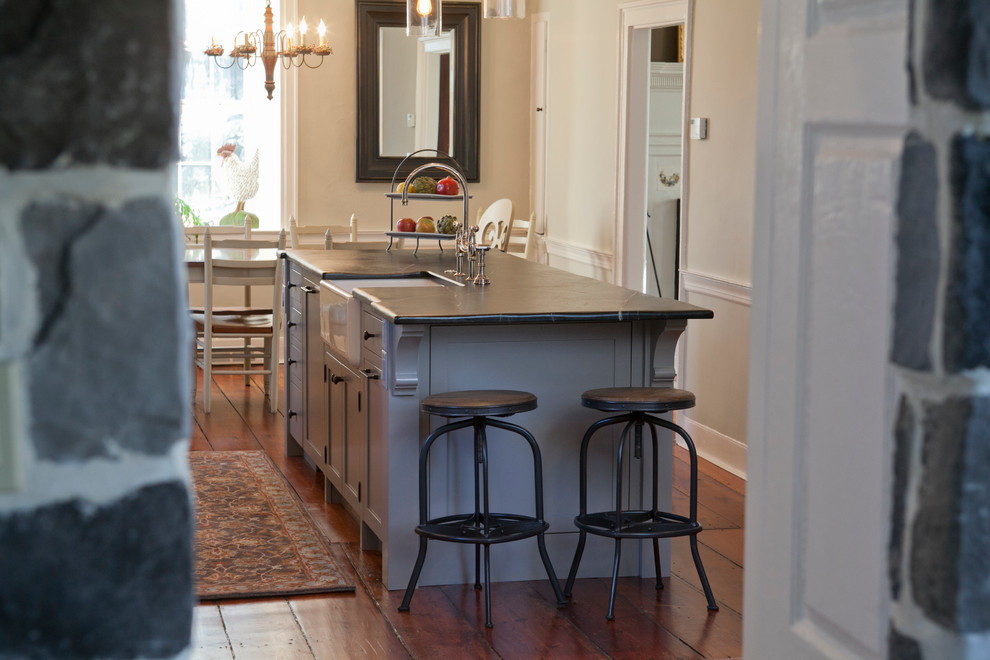 Example of a large farmhouse galley medium tone wood floor eat-in kitchen design in Philadelphia with a farmhouse sink, shaker cabinets, gray cabinets, soapstone countertops, stainless steel appliances and an island