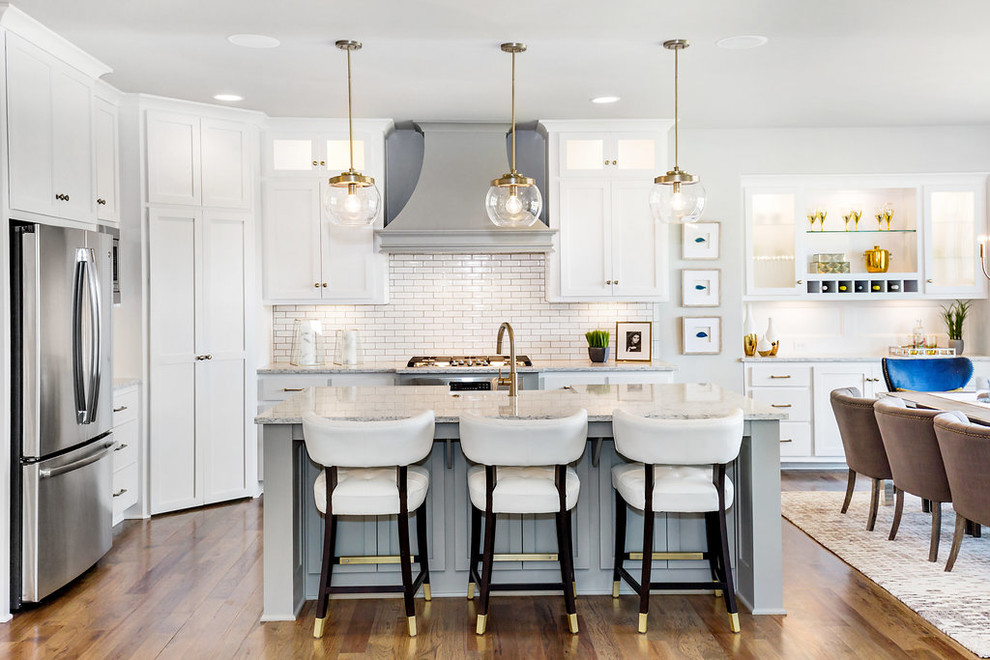 This is an example of a traditional kitchen/diner in Kansas City with shaker cabinets, white cabinets, white splashback, metro tiled splashback, stainless steel appliances, medium hardwood flooring, an island and grey worktops.