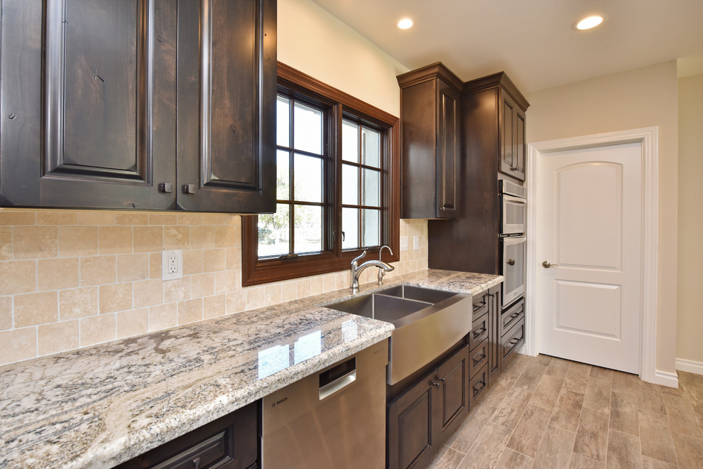 Modern inredning av ett stort kök, med en rustik diskho, luckor med upphöjd panel, skåp i mörkt trä, granitbänkskiva, beige stänkskydd, stänkskydd i stenkakel, integrerade vitvaror, vinylgolv, en köksö och brunt golv