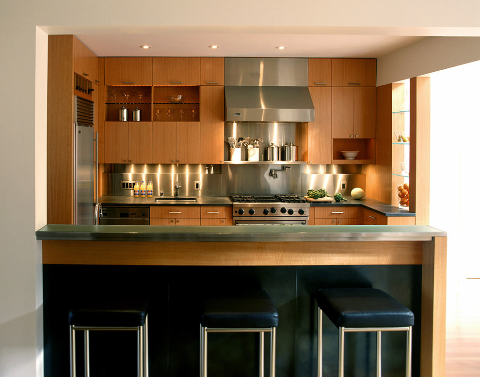 Exemple d'une cuisine tendance en L et bois brun avec un électroménager en acier inoxydable, un placard à porte plane et une crédence métallisée.