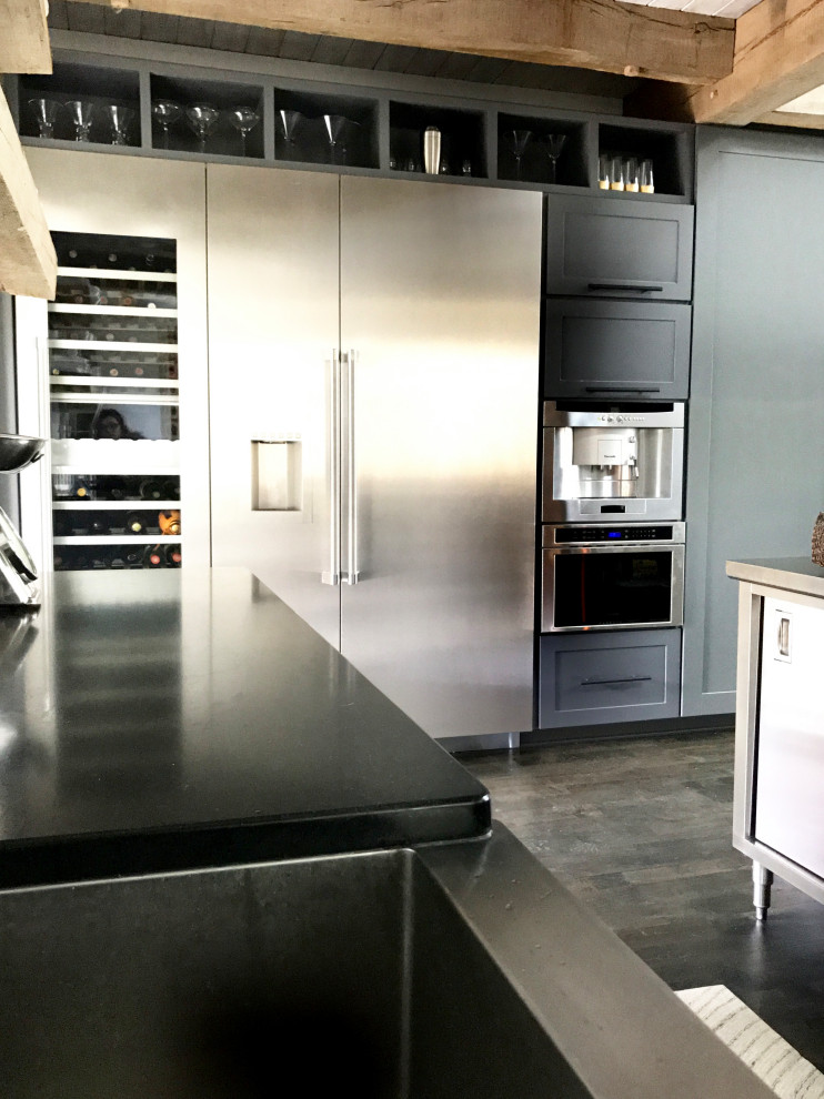 This is an example of a medium sized urban l-shaped open plan kitchen in Raleigh with a belfast sink, shaker cabinets, grey cabinets, engineered stone countertops, stainless steel appliances, dark hardwood flooring, a breakfast bar, brown floors and black worktops.