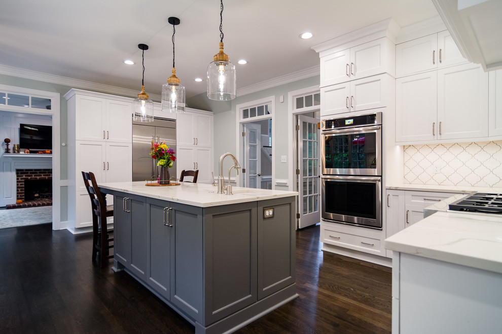 Example of a transitional medium tone wood floor and brown floor kitchen pantry design in Raleigh with white cabinets, quartz countertops, orange backsplash, porcelain backsplash, stainless steel appliances, an island and white countertops