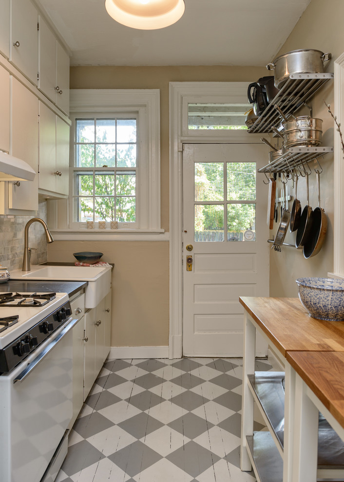 Exemple d'une petite cuisine linéaire chic avec un évier de ferme, un placard à porte plane, des portes de placard blanches, un plan de travail en stéatite, une crédence grise, une crédence en carrelage de pierre, un électroménager blanc, parquet peint et aucun îlot.