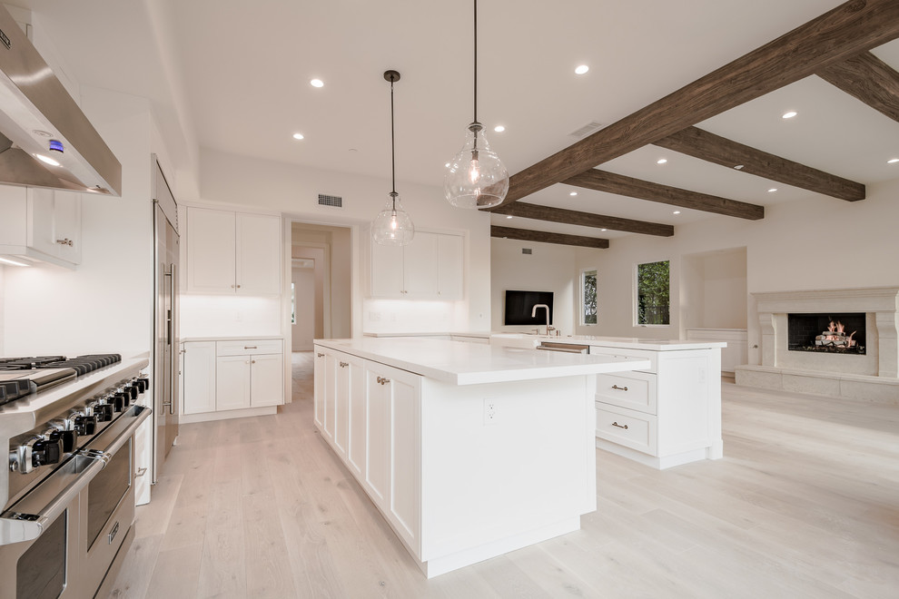 Large danish u-shaped light wood floor and beige floor open concept kitchen photo in Los Angeles with a farmhouse sink, shaker cabinets, white cabinets, quartz countertops, white backsplash, ceramic backsplash, stainless steel appliances, an island and white countertops