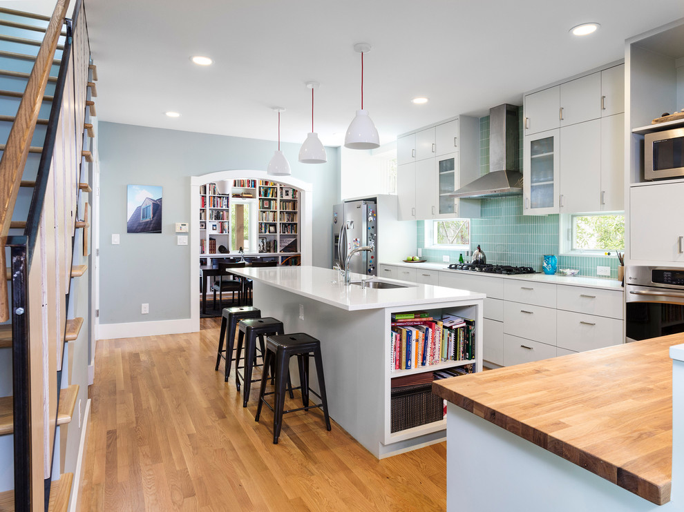 Inspiration for a contemporary l-shaped medium tone wood floor kitchen remodel in Austin with an undermount sink, flat-panel cabinets, green backsplash, stainless steel appliances, quartz countertops, glass tile backsplash, an island and white cabinets