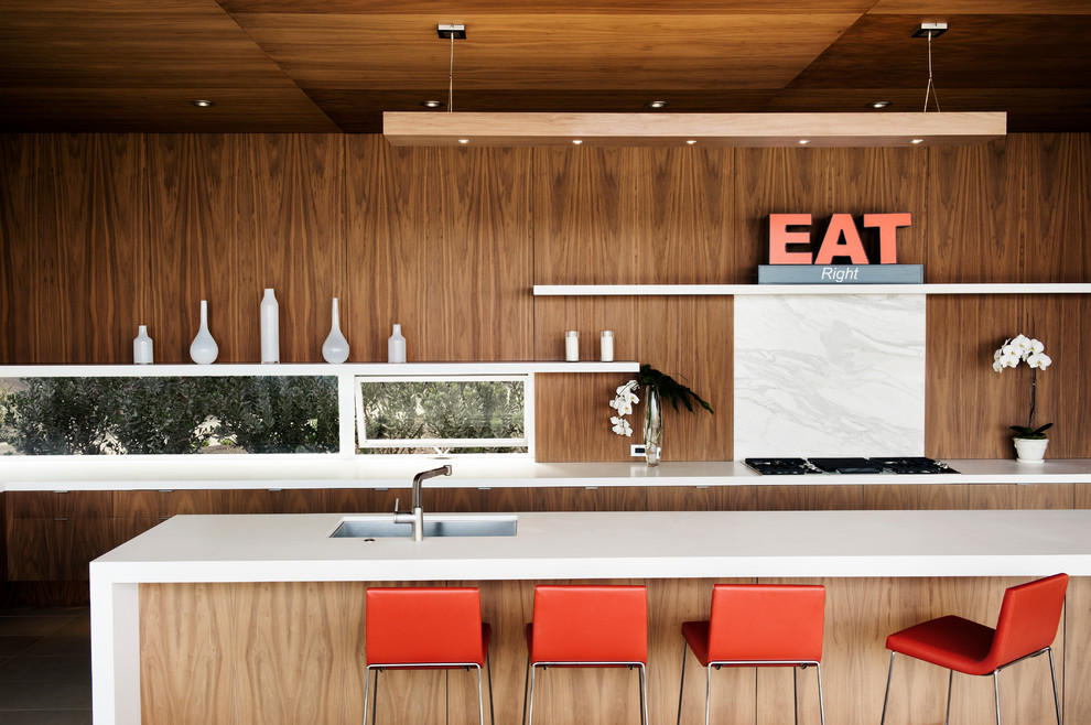 На фото: кухня в современном стиле с врезной мойкой, плоскими фасадами, темными деревянными фасадами, белым фартуком и фартуком из каменной плиты