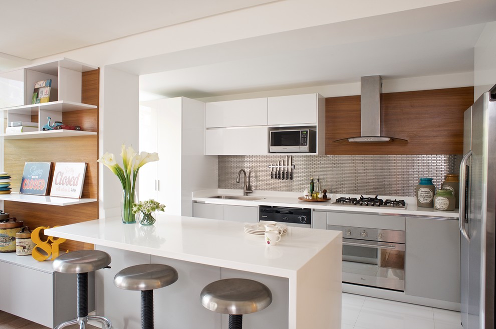 Exempel på ett modernt vit vitt l-kök, med en enkel diskho, släta luckor, vita skåp, stänkskydd med metallisk yta, stänkskydd i metallkakel, rostfria vitvaror, en halv köksö och vitt golv
