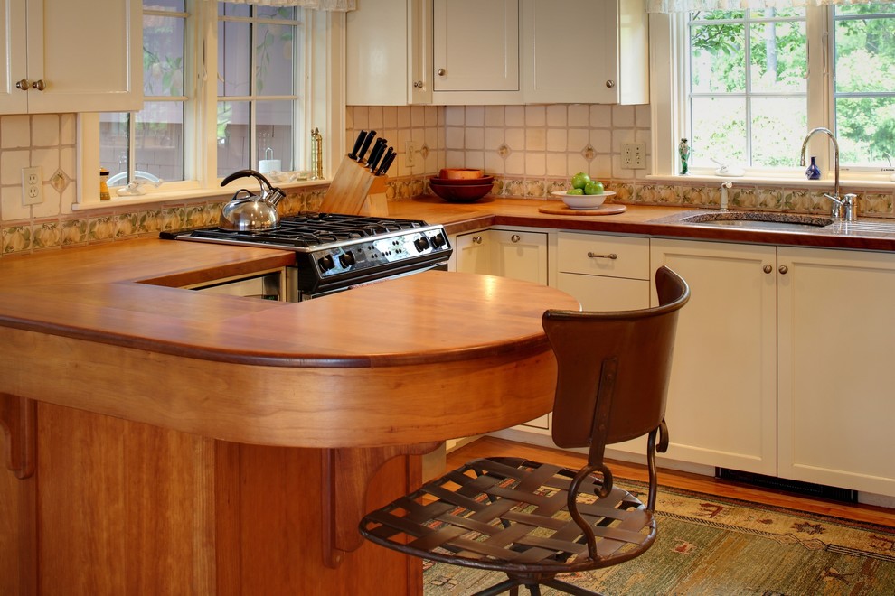 Example of a mid-sized classic u-shaped medium tone wood floor and brown floor kitchen design in Portland Maine with a single-bowl sink, shaker cabinets, white cabinets, wood countertops, white backsplash, ceramic backsplash, stainless steel appliances and a peninsula