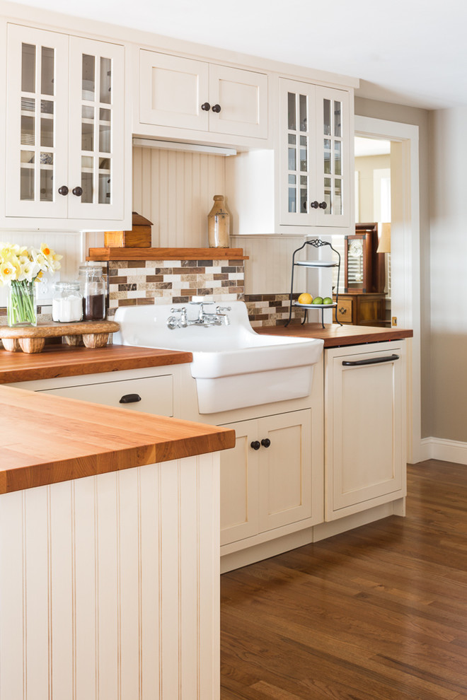 Coastal kitchen in Portland Maine with a belfast sink, shaker cabinets, white cabinets, wood worktops, brown splashback, medium hardwood flooring and a breakfast bar.