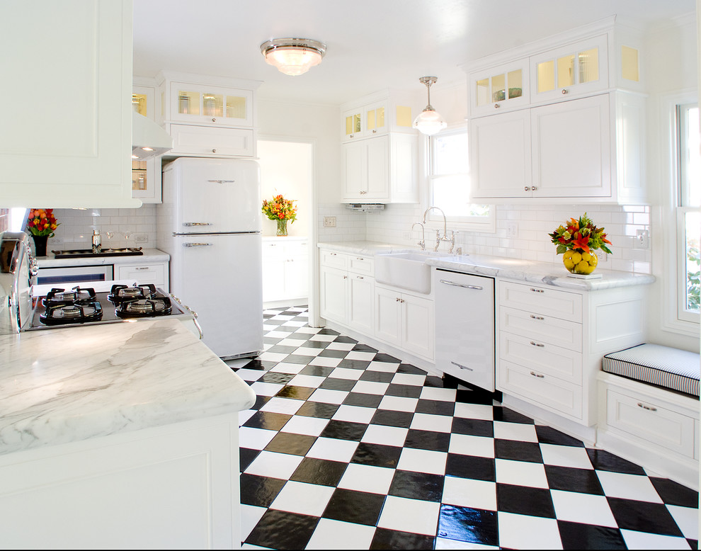 Elegant u-shaped multicolored floor enclosed kitchen photo in San Francisco with a farmhouse sink, marble countertops, white appliances, white cabinets, white backsplash and subway tile backsplash