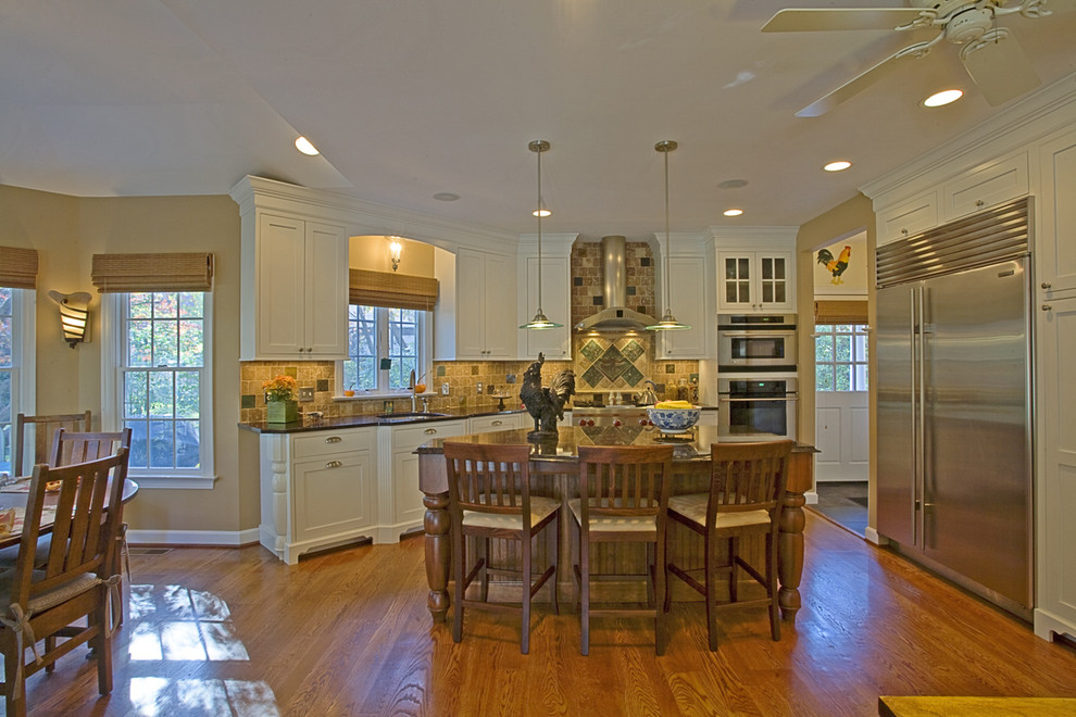 Cette photo montre une cuisine chic avec un placard à porte shaker, des portes de placard blanches, une crédence beige et un électroménager en acier inoxydable.