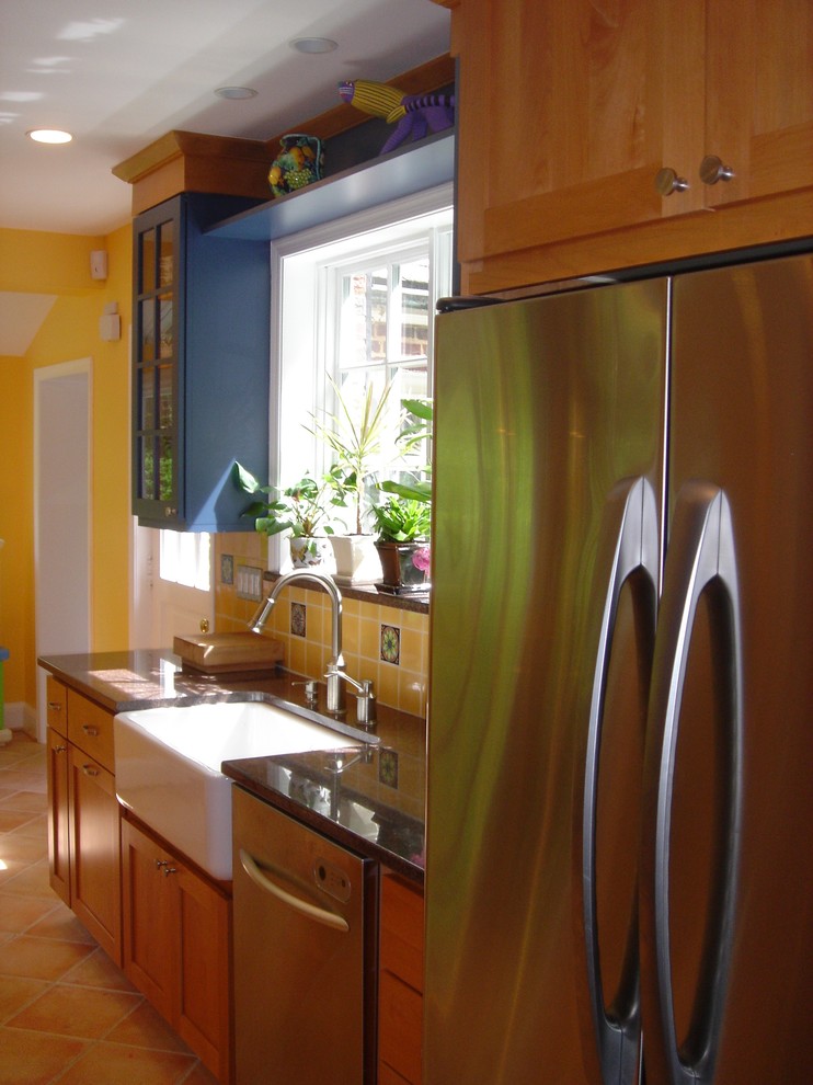 Exemple d'une cuisine chic avec un placard à porte vitrée, un électroménager en acier inoxydable, un évier de ferme, des portes de placard bleues et une crédence jaune.