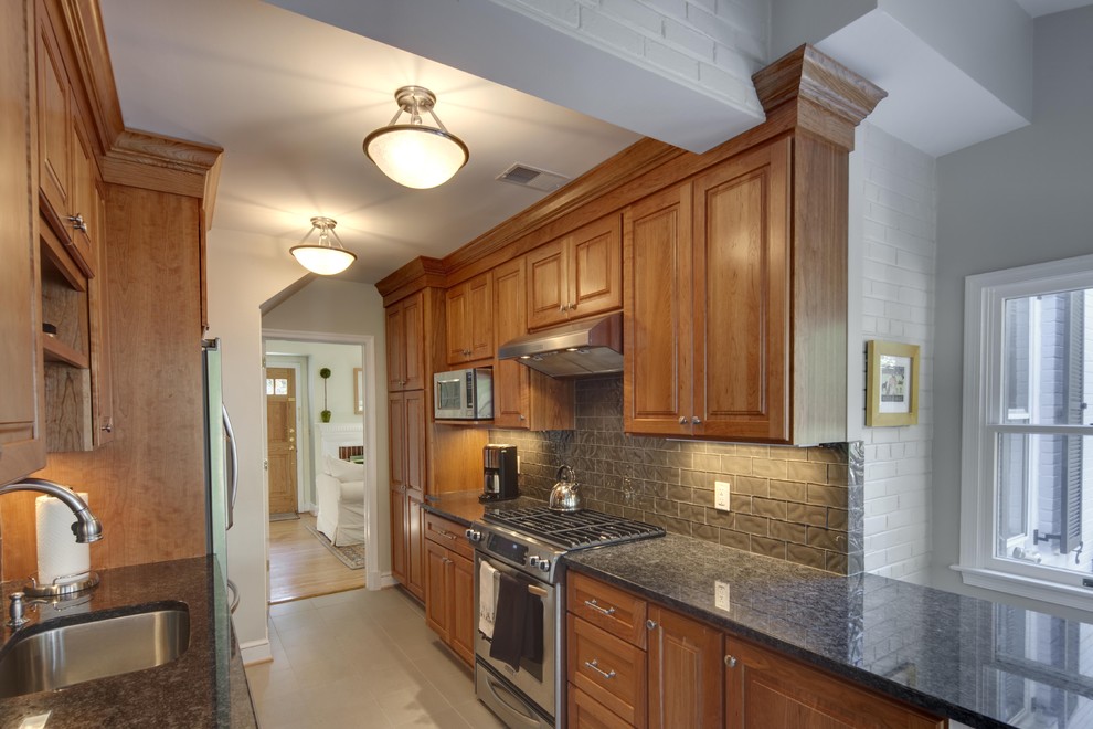 Example of a trendy galley enclosed kitchen design in DC Metro with stainless steel appliances, granite countertops, an undermount sink, raised-panel cabinets, medium tone wood cabinets, gray backsplash and subway tile backsplash