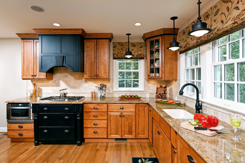 Klassisk inredning av ett kök, med luckor med infälld panel, en undermonterad diskho, granitbänkskiva, skåp i mellenmörkt trä, beige stänkskydd och rostfria vitvaror