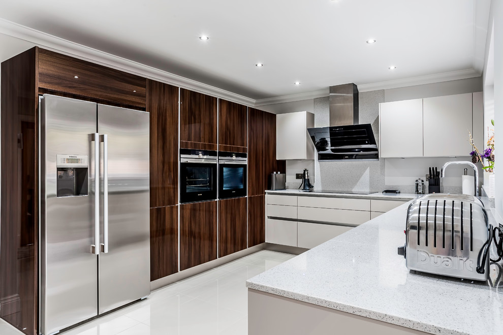 This is an example of a medium sized modern u-shaped kitchen/diner in Essex with a submerged sink, flat-panel cabinets, white cabinets, quartz worktops, white splashback, stone slab splashback, black appliances, porcelain flooring and a breakfast bar.