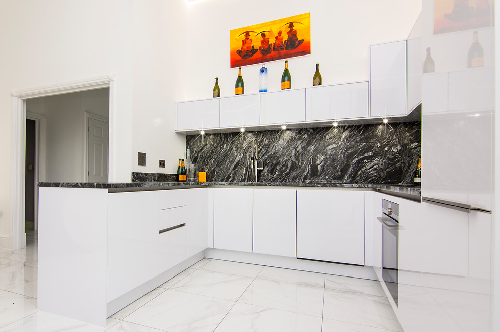 Foto på ett litet funkis svart kök, med en integrerad diskho, släta luckor, vita skåp, granitbänkskiva, svart stänkskydd, stänkskydd i sten, svarta vitvaror, klinkergolv i porslin och vitt golv