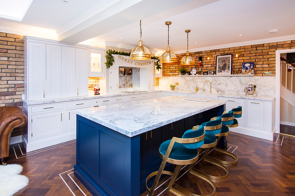 Inspiration for a large classic l-shaped kitchen in Essex with a belfast sink, shaker cabinets, white cabinets, marble worktops, white splashback, marble splashback, dark hardwood flooring, an island, brown floors and white worktops.