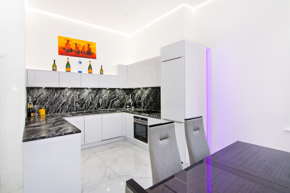 Small minimalist u-shaped porcelain tile and white floor open concept kitchen photo in Essex with an integrated sink, flat-panel cabinets, white cabinets, granite countertops, black backsplash, stone slab backsplash, black appliances, no island and black countertops