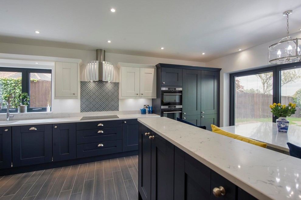 Photo of a medium sized contemporary l-shaped kitchen/diner in Other with a submerged sink, shaker cabinets, blue cabinets, quartz worktops, grey splashback, glass sheet splashback, stainless steel appliances, porcelain flooring, a breakfast bar, grey floors and white worktops.