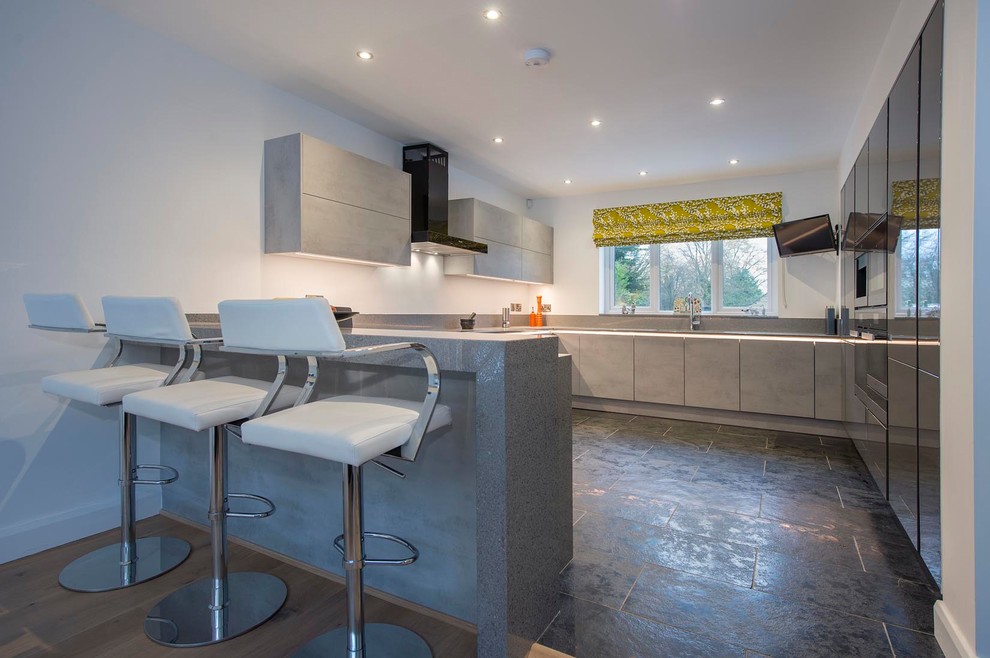 This is an example of a large contemporary u-shaped open plan kitchen in Other with a submerged sink, flat-panel cabinets, grey cabinets, quartz worktops, grey splashback, stone slab splashback, black appliances, ceramic flooring, a breakfast bar, grey floors and grey worktops.
