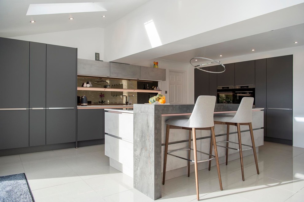 Design ideas for a medium sized contemporary l-shaped open plan kitchen in Other with a submerged sink, flat-panel cabinets, grey cabinets, quartz worktops, glass sheet splashback, black appliances, porcelain flooring, an island, beige worktops, metallic splashback and beige floors.