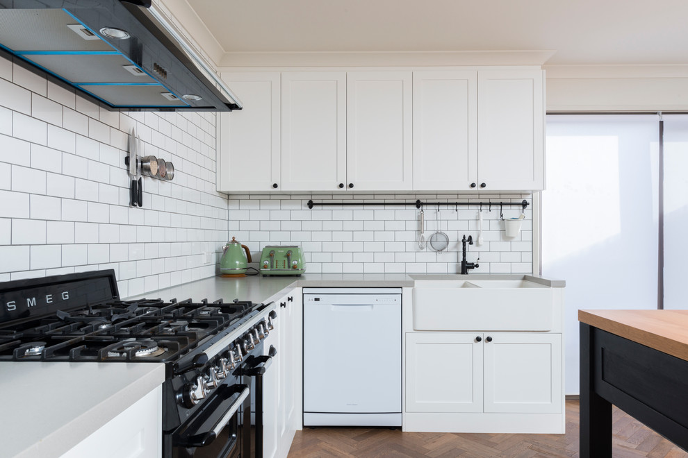 Foto på ett mellanstort eklektiskt kök, med en rustik diskho, skåp i shakerstil, vita skåp, bänkskiva i kvarts, vitt stänkskydd, stänkskydd i tunnelbanekakel, svarta vitvaror, mellanmörkt trägolv och en köksö