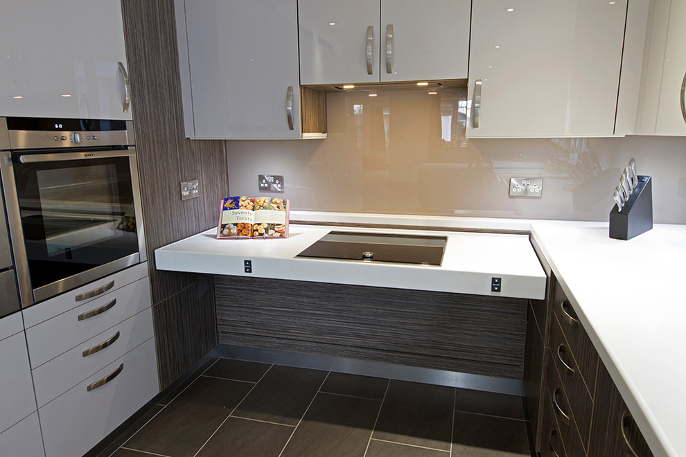 Small trendy u-shaped porcelain tile and brown floor open concept kitchen photo in Buckinghamshire with an integrated sink, flat-panel cabinets, beige cabinets, solid surface countertops, beige backsplash, glass sheet backsplash, stainless steel appliances and no island