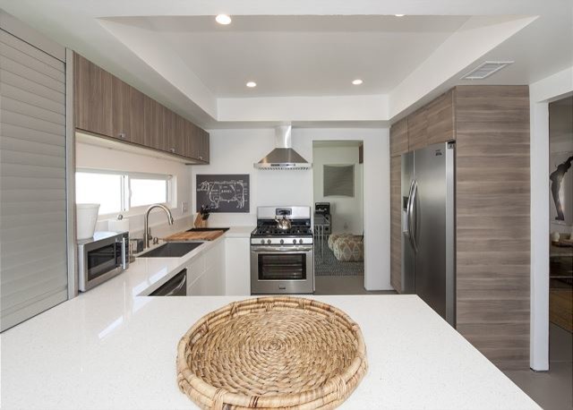 Medium sized modern l-shaped kitchen/diner in Los Angeles with a submerged sink, flat-panel cabinets, grey cabinets, engineered stone countertops, white splashback, stone slab splashback, stainless steel appliances, concrete flooring and an island.