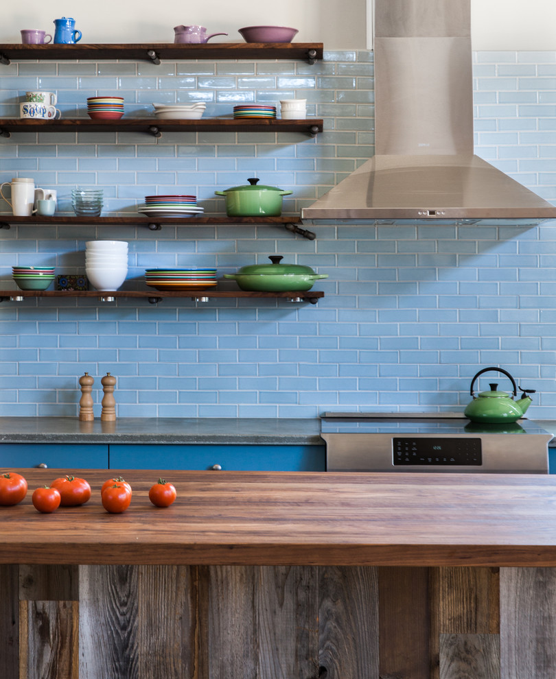 Diseño de cocina campestre con puertas de armario azules, encimera de cemento, salpicadero azul, salpicadero de azulejos de cerámica, electrodomésticos de acero inoxidable y una isla