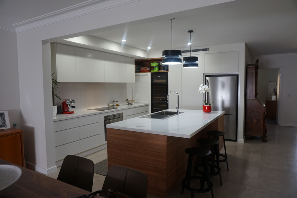 Modern inredning av ett mellanstort kök, med en nedsänkt diskho, vita skåp, bänkskiva i kvarts, vitt stänkskydd, stänkskydd i porslinskakel, rostfria vitvaror, klinkergolv i keramik och en köksö