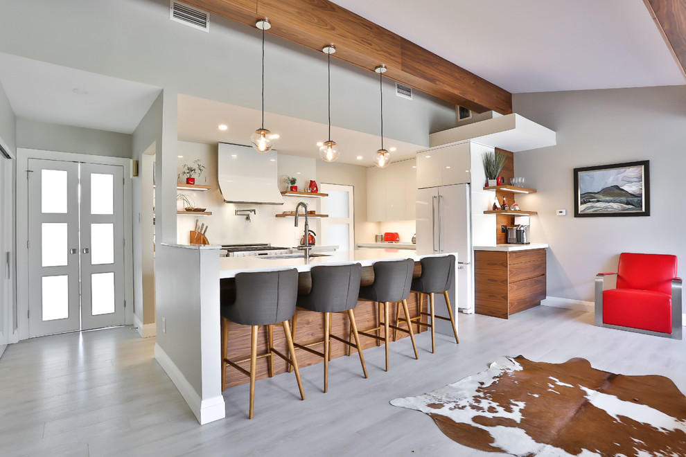 Medium sized midcentury l-shaped open plan kitchen in Toronto with a submerged sink, flat-panel cabinets, white cabinets, engineered stone countertops, white splashback, stone slab splashback, white appliances, vinyl flooring, an island and beige floors.