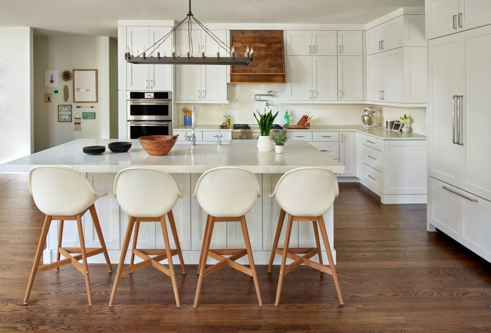 Inspiration for a transitional l-shaped dark wood floor and brown floor kitchen remodel in Denver with a farmhouse sink, shaker cabinets, white cabinets, beige backsplash, mosaic tile backsplash, stainless steel appliances, an island and beige countertops