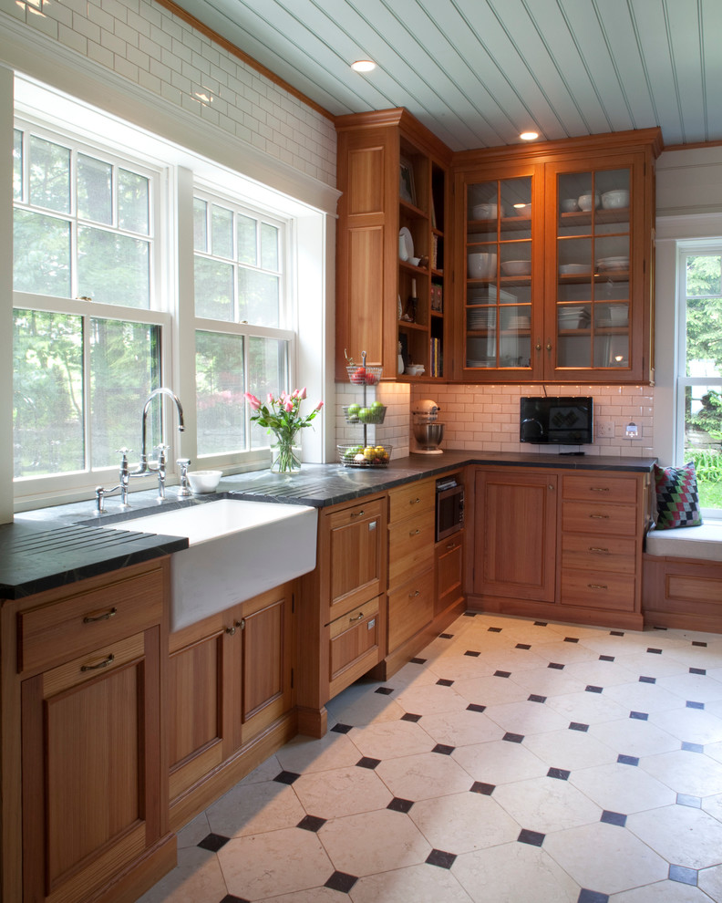 Rural kitchen in Portland Maine with a belfast sink, shaker cabinets, medium wood cabinets, soapstone worktops, white splashback, metro tiled splashback, an island and white floors.